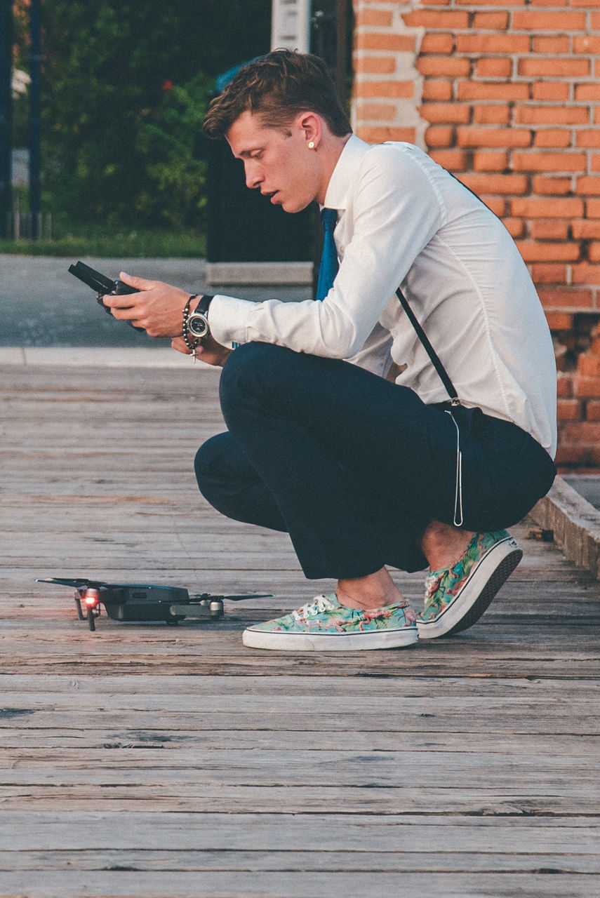 Side view of man crouching by drone on floorboard