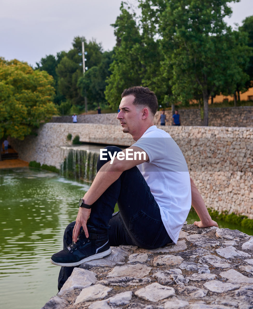 Side view of man sitting on retaining wall