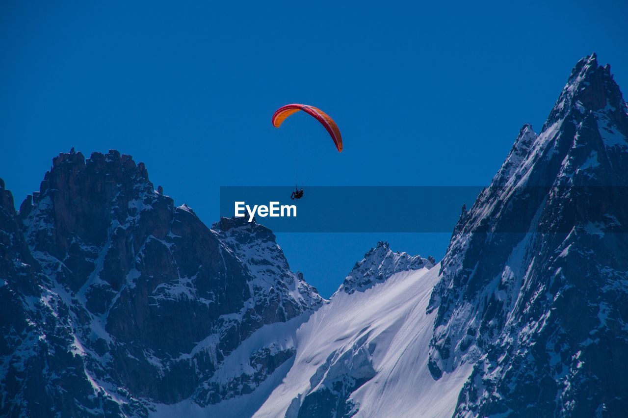 PERSON PARAGLIDING OVER SNOWCAPPED MOUNTAINS