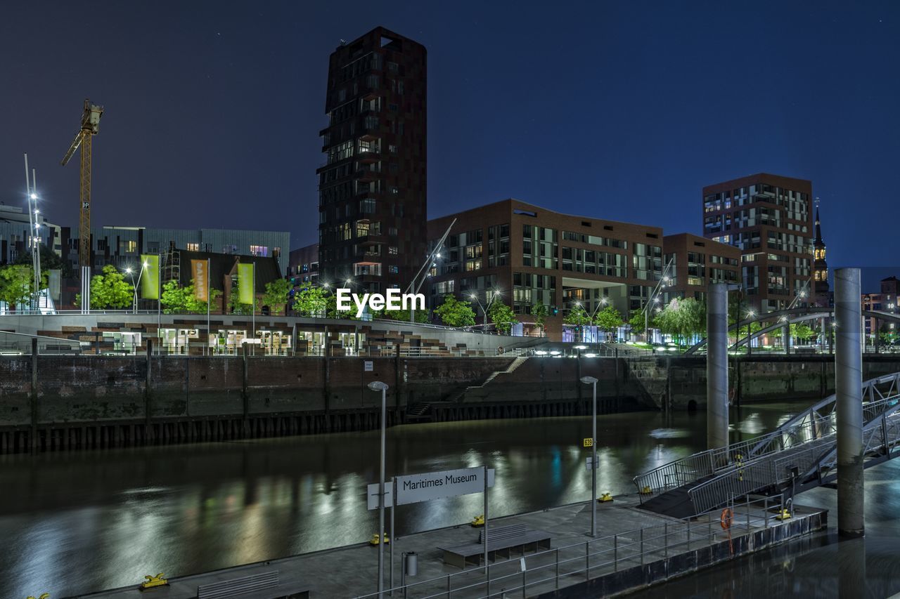 Canal by illuminated buildings against clear sky at night