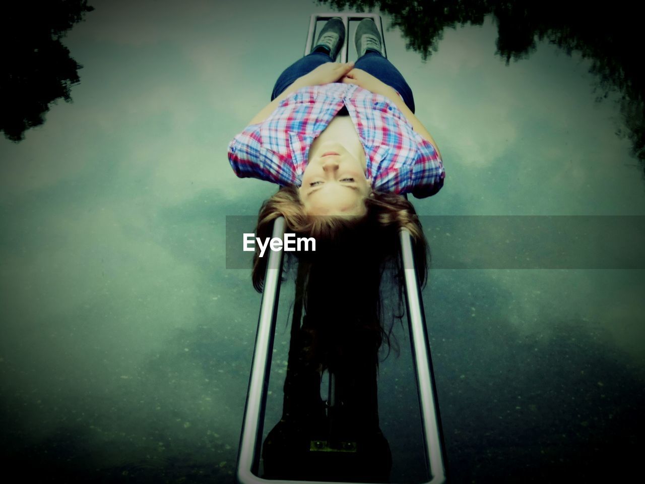 High angle view of woman relaxing on metal structure over pond