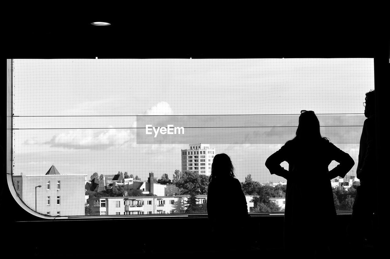 SILHOUETTE WOMAN STANDING BY WINDOW IN CITY