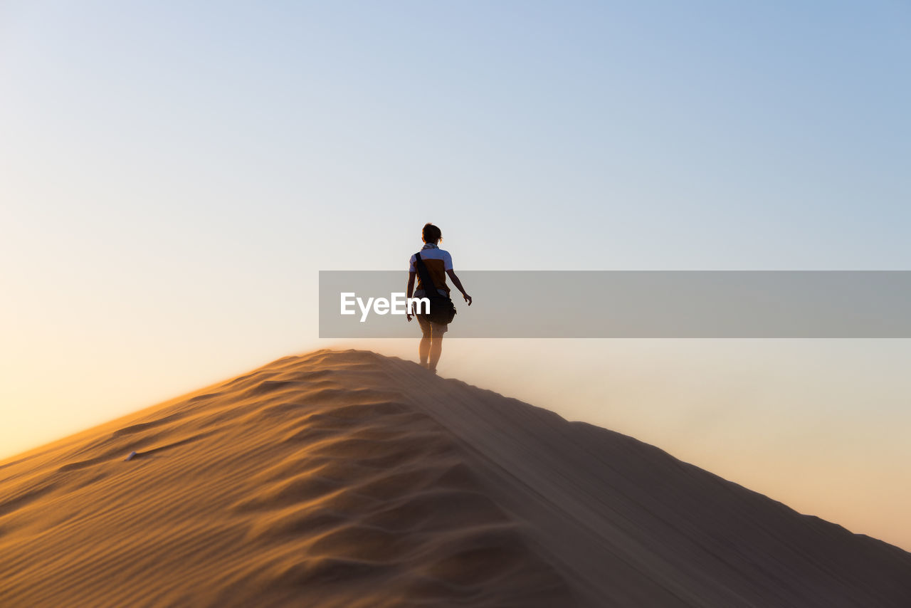Rear view of woman walking on desert against sky