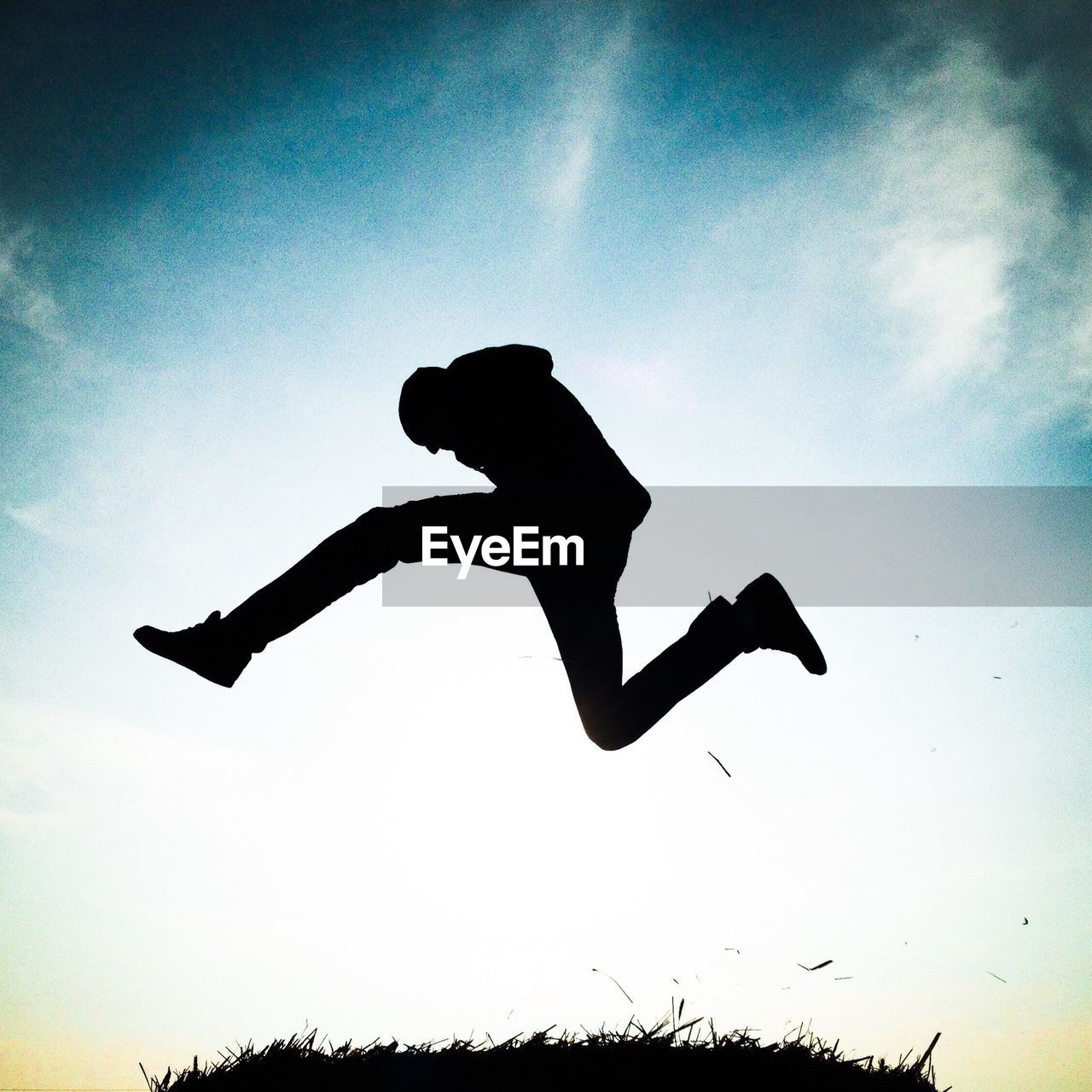 Silhouette man jumping above grass against sky