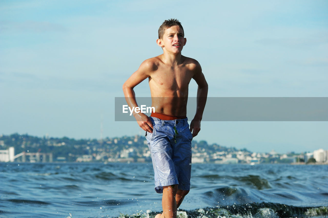 Shirtless boy walking in sea against sky