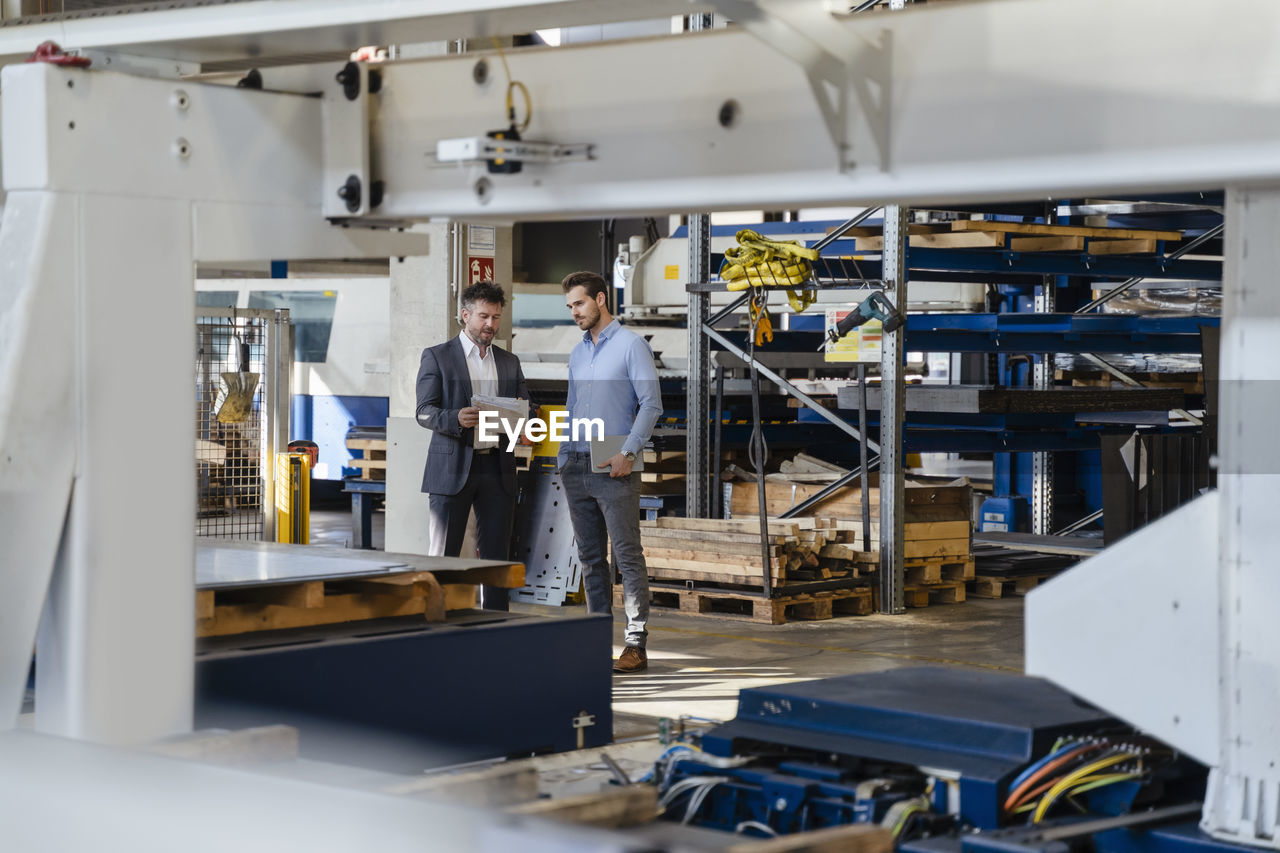 Businessman holding paper while explaining to colleague at factory