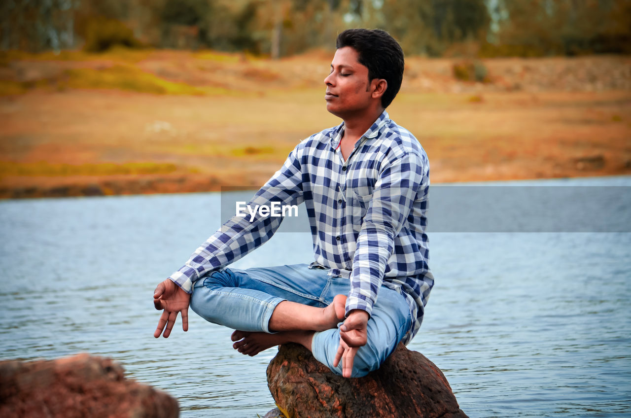 Man doing yoga while sitting on rock at lake