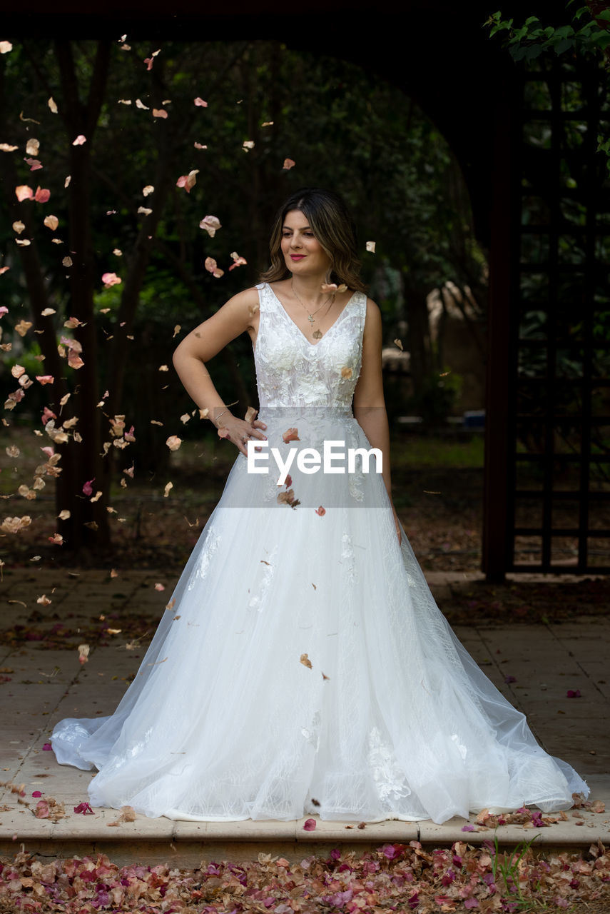 Pregnant happy bride wearing white wedding dress posing outdoor.