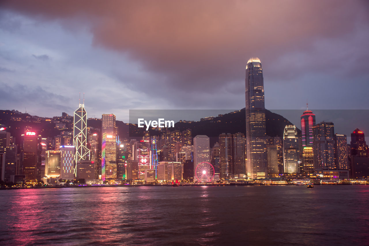 Illuminated buildings by river against sky at night