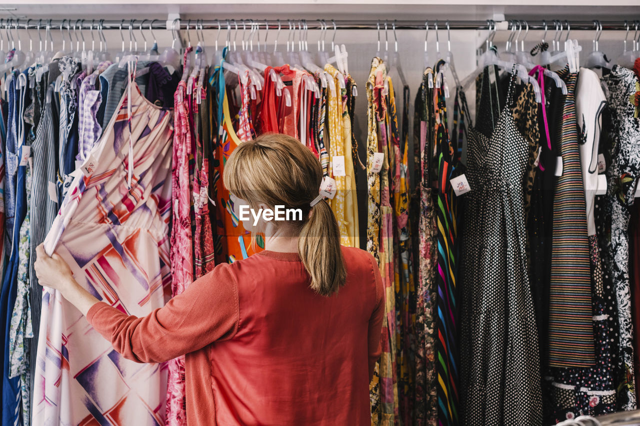 Woman looking at dress hanging on rack while standing at store