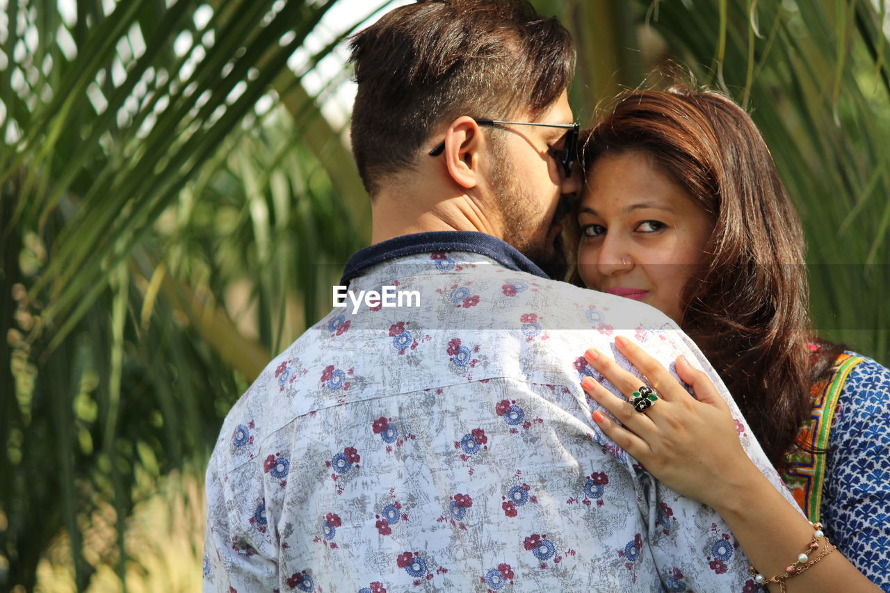 Portrait of woman embracing man while standing by tree