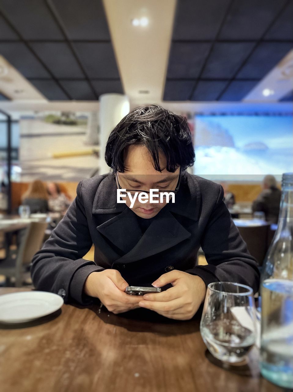 Portrait of young asian man using mobile phone at table in restaurant.