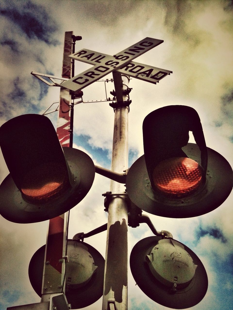 Railway crossing sign and stop light against sky