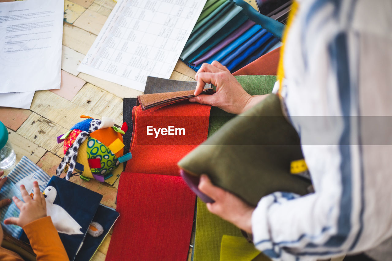 High angle view of fashion designer choosing textile from colorful swatch while baby girl playing with fabric picture bo