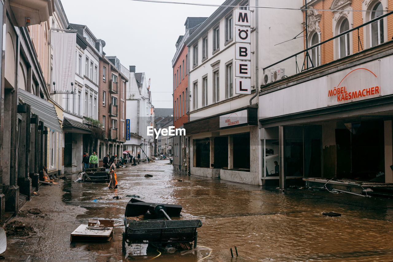 WET STREET AMIDST BUILDINGS AGAINST SKY