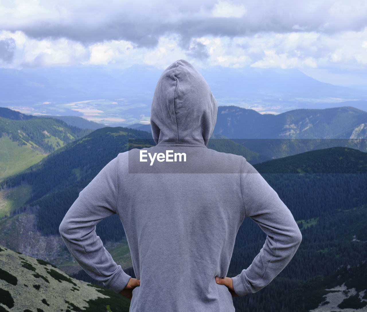 A boy in a sweatshirt from behind on top of a hill enjoys the view