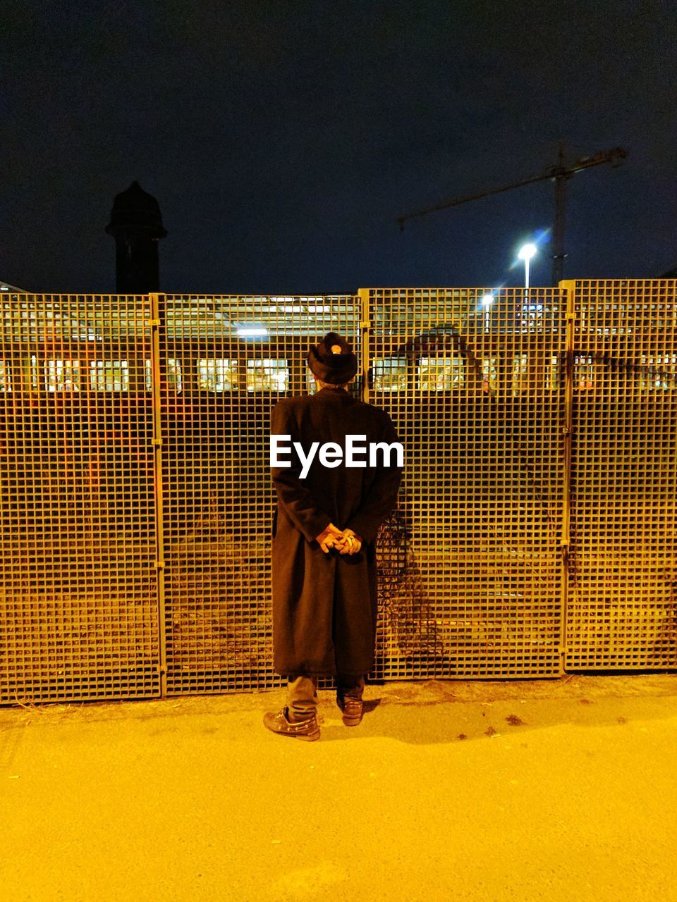 FULL LENGTH REAR VIEW OF MAN STANDING AGAINST WALL AT NIGHT