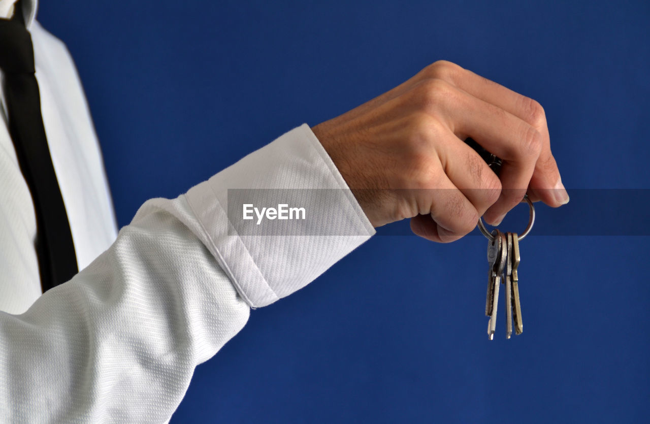 Midsection of businessman holding keys against blue background