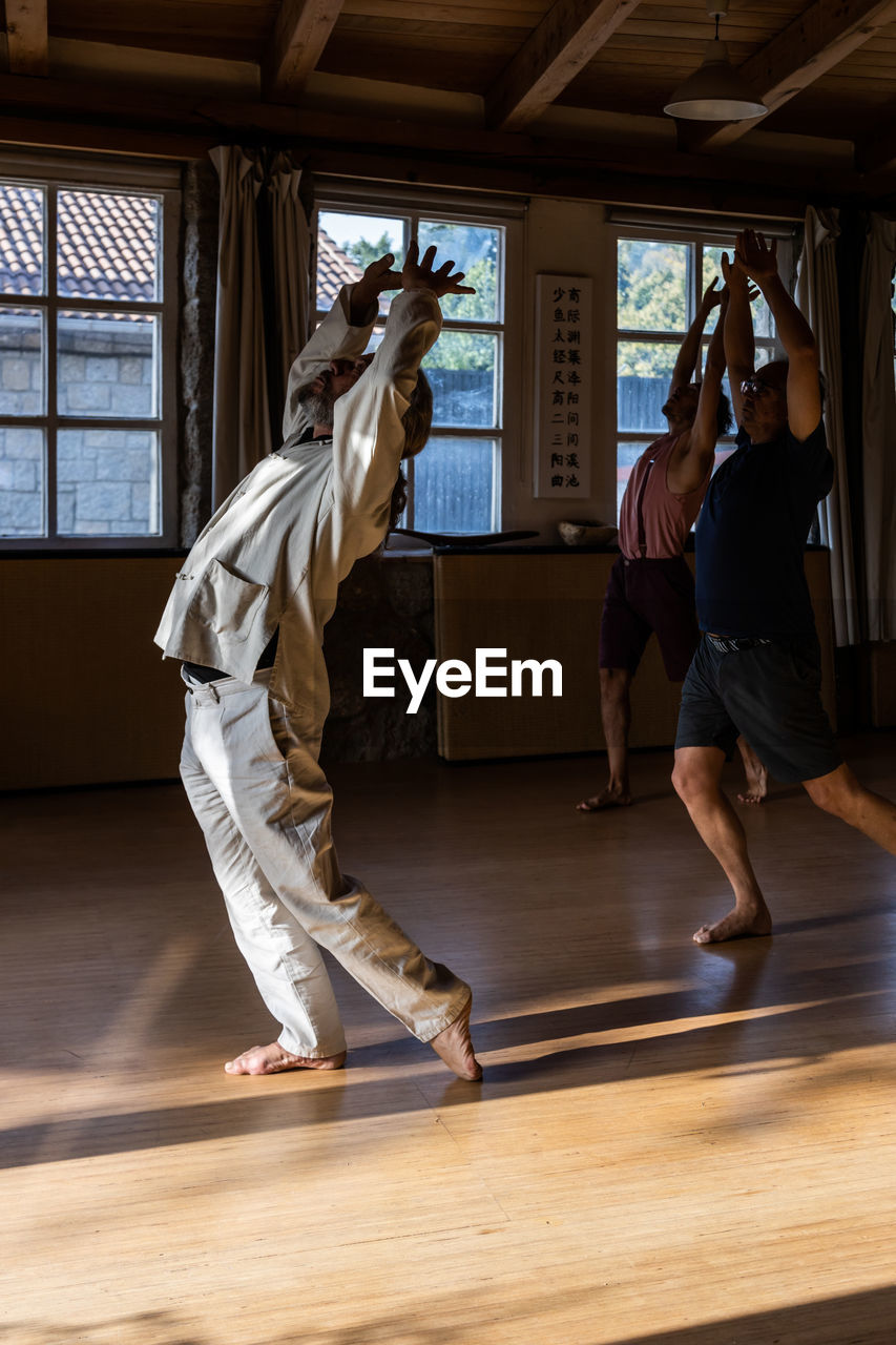 Full body side view of unrecognizable male instructor doing chi kung or qigong movement with arms raised during practice with students