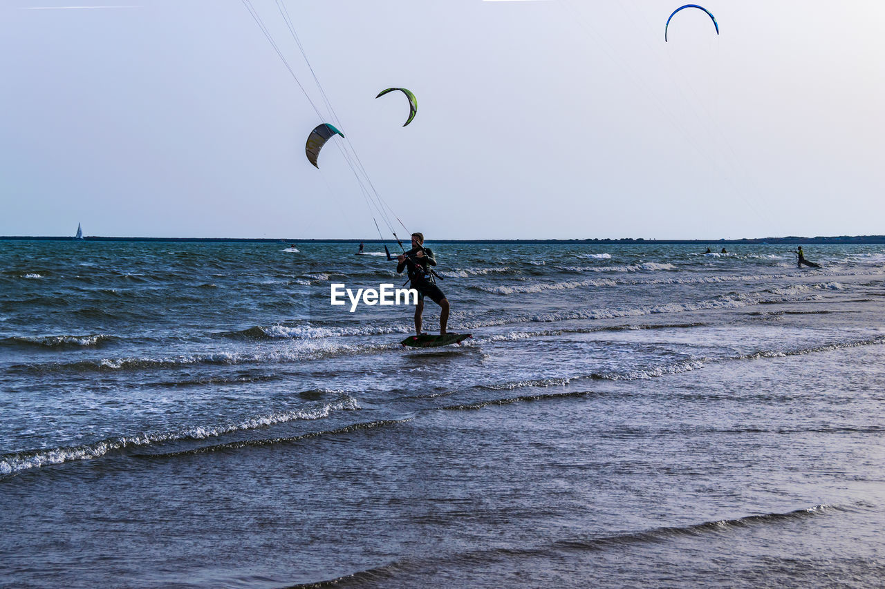 MAN SURFING IN SEA AGAINST SKY AT BEACH