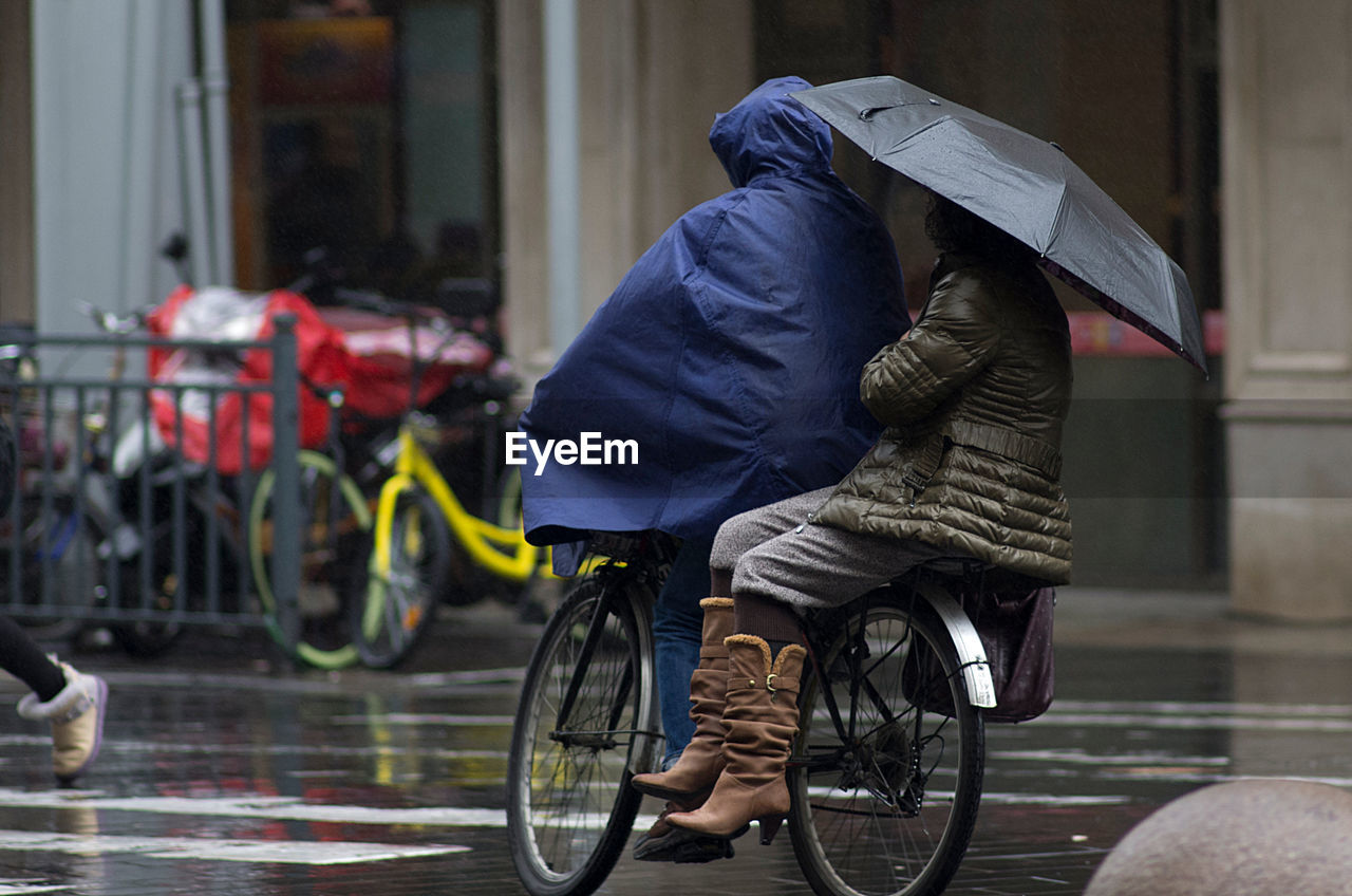 Midsection of two people on a bicycle on a rainy day