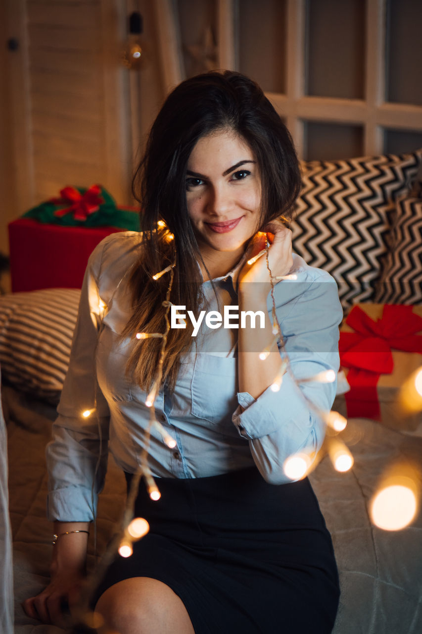 Portrait of smiling young woman with illuminated string light at home