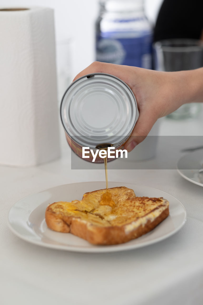 Midsection of person pouring maple syrup on french toast