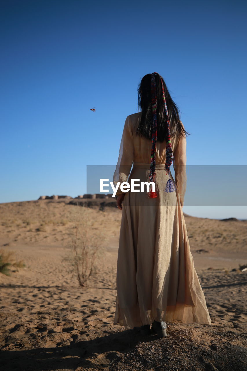 Rear view of woman standing on land against clear blue sky