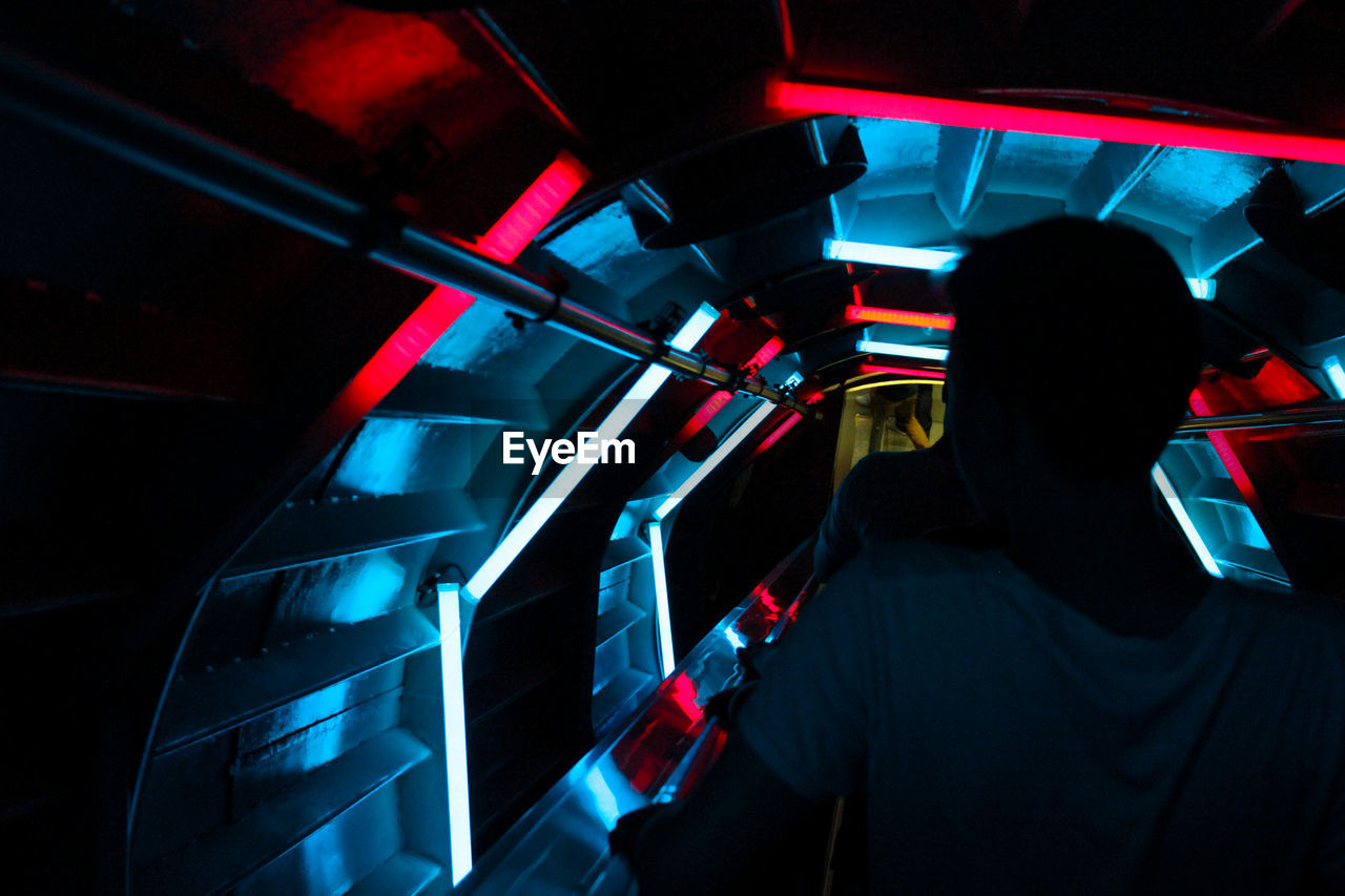 REAR VIEW OF PEOPLE TRAVELING IN ILLUMINATED TRAIN