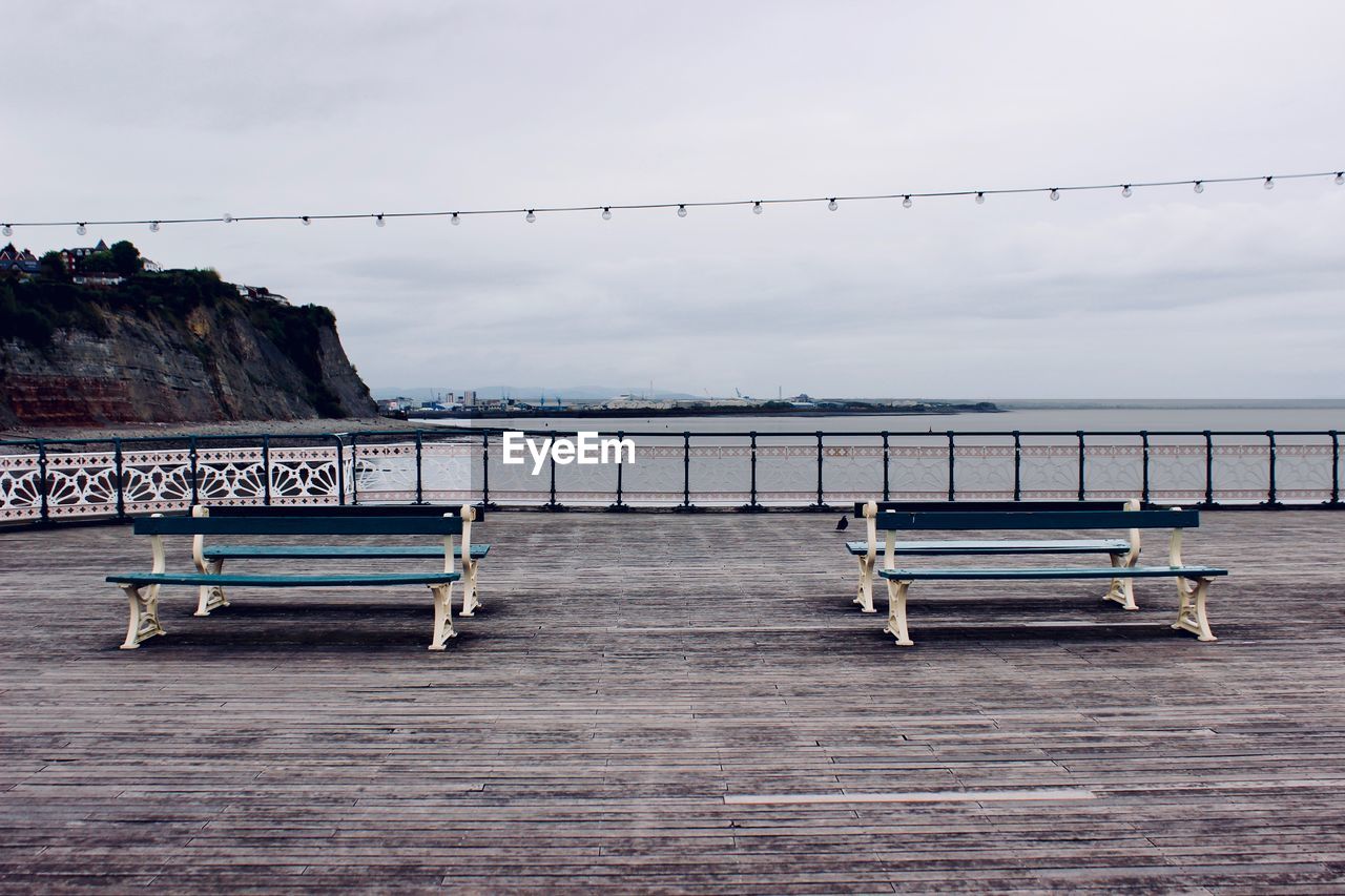 Empty bench by sea against sky