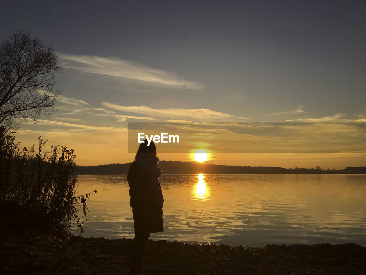 Silhouette woman standing by lake against sky during sunset