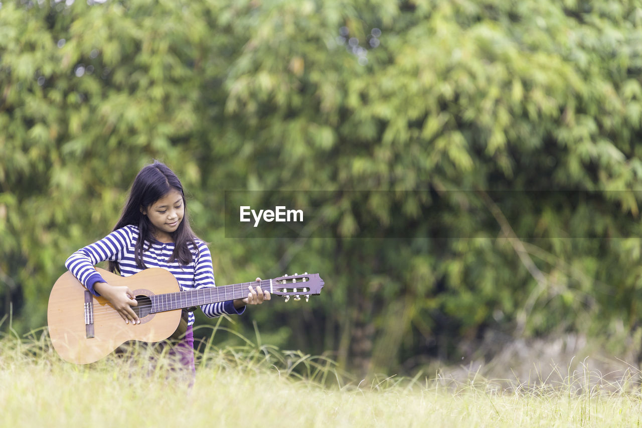 Cute smiling girl playing guitar sitting outdoors