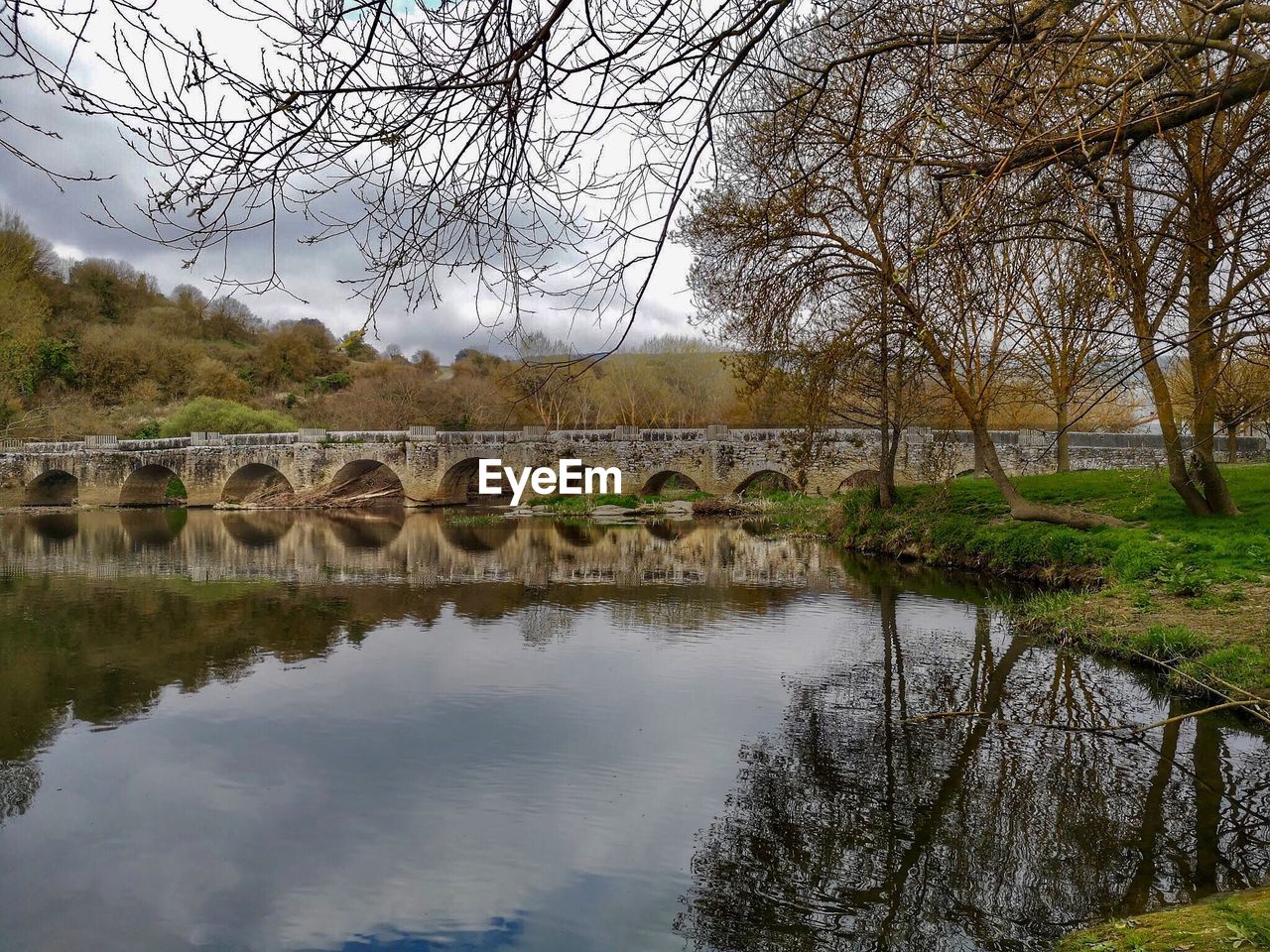 BRIDGE OVER RIVER BY BARE TREES AGAINST SKY