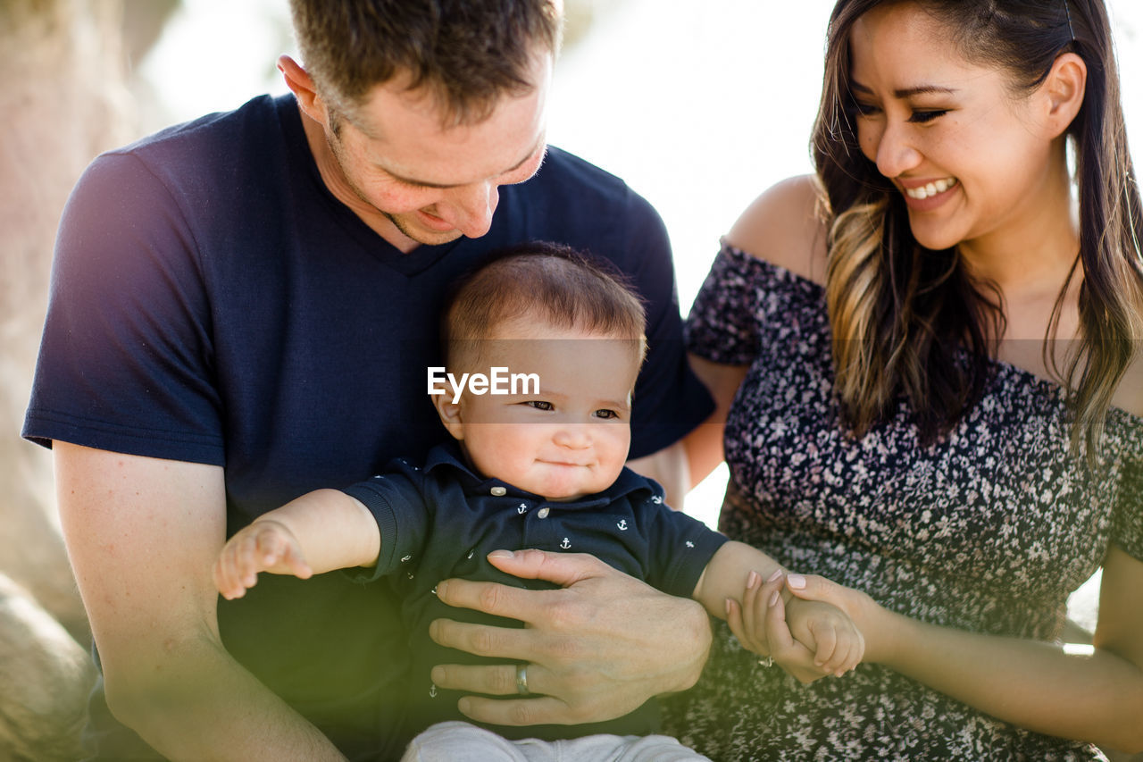 Parents sitting under tree smiling at infant son