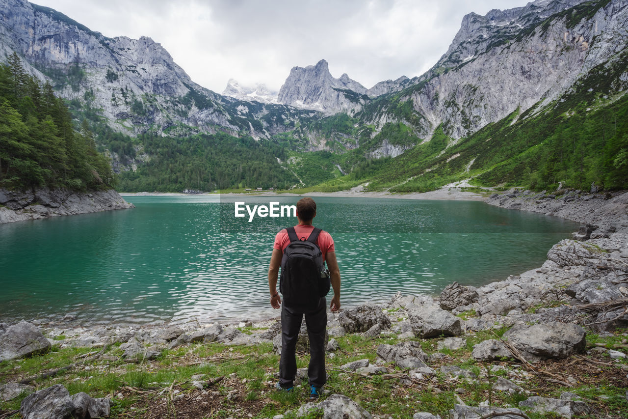 Man traveler enjoying view of dachstein peak mountains on a upper gosau lake. gosau, austria, europe