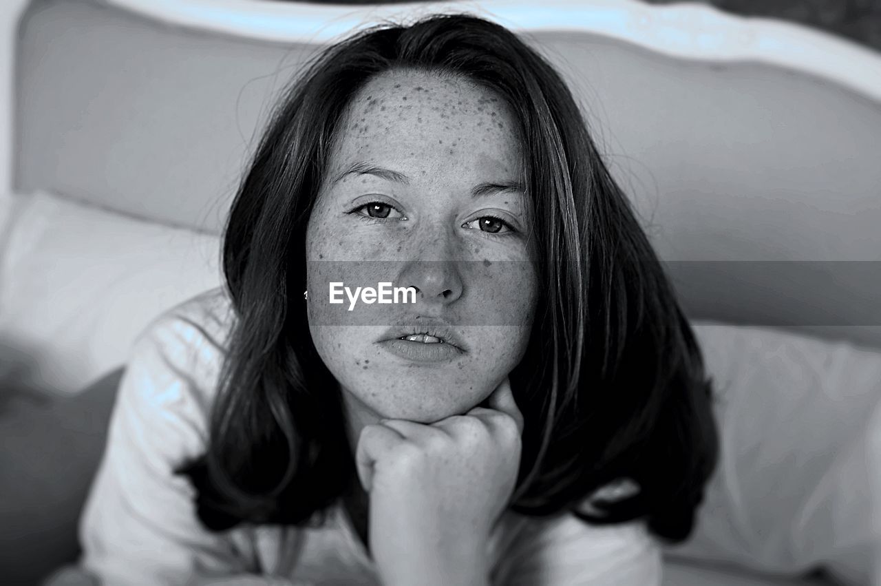 Portrait of young woman with freckle on her face while resting on bed