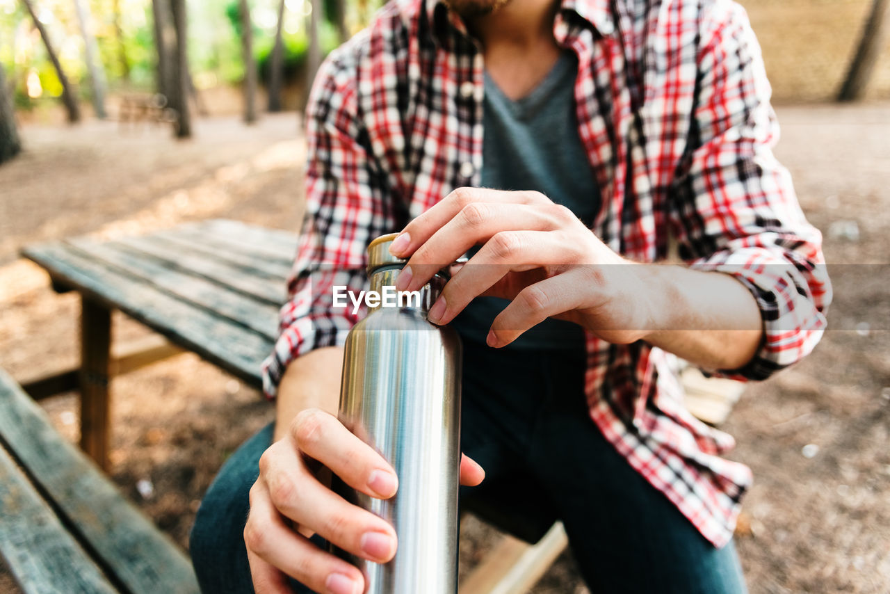 Midsection of man holding bottle outdoors