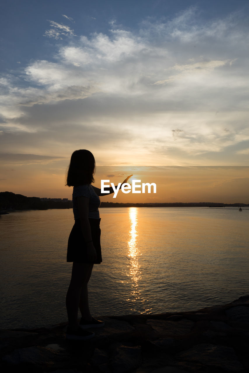 SILHOUETTE WOMAN STANDING ON BEACH AGAINST ORANGE SKY