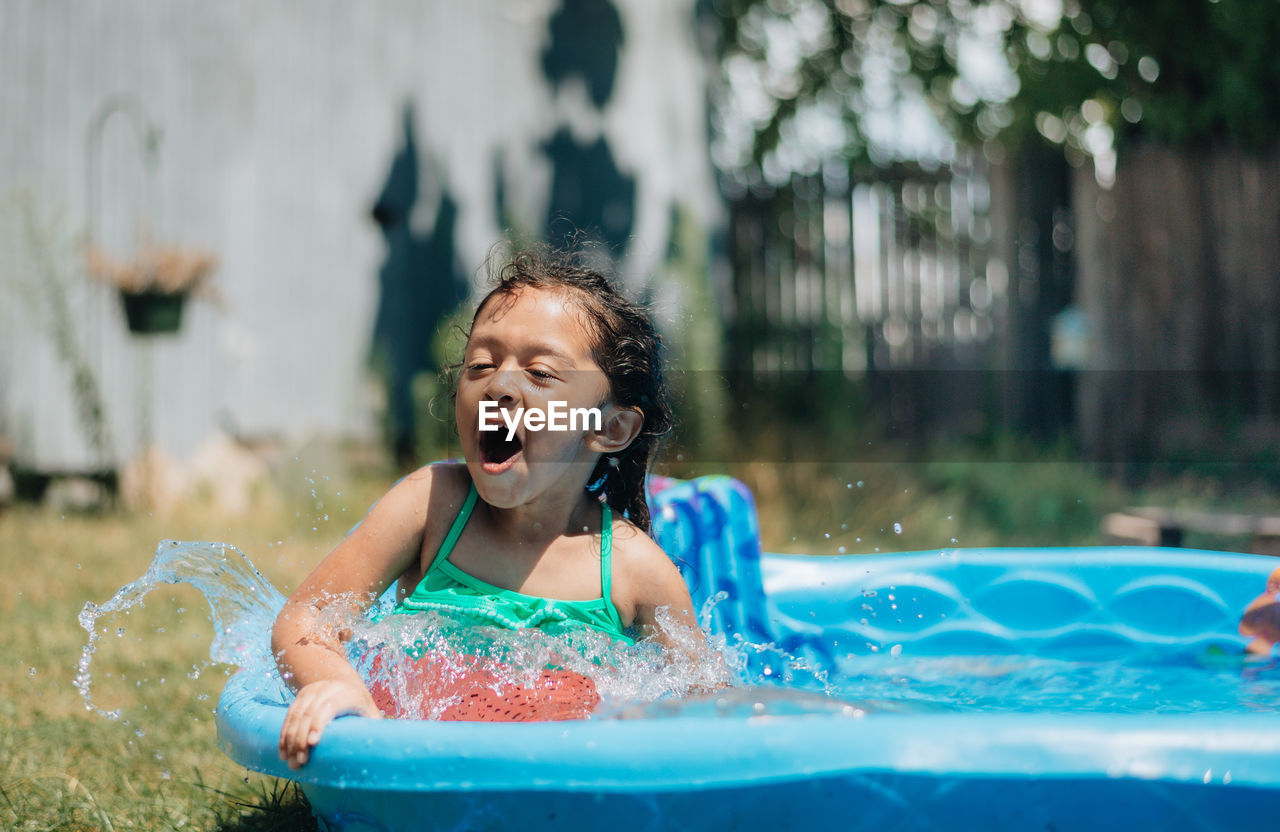 Mixed race young girl at home having fun on hot summer day in kiddie pool