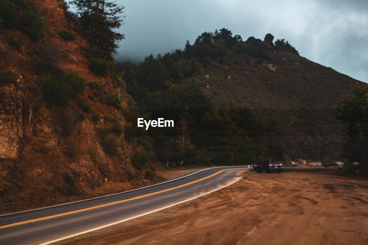 Road amidst trees and mountains against sky