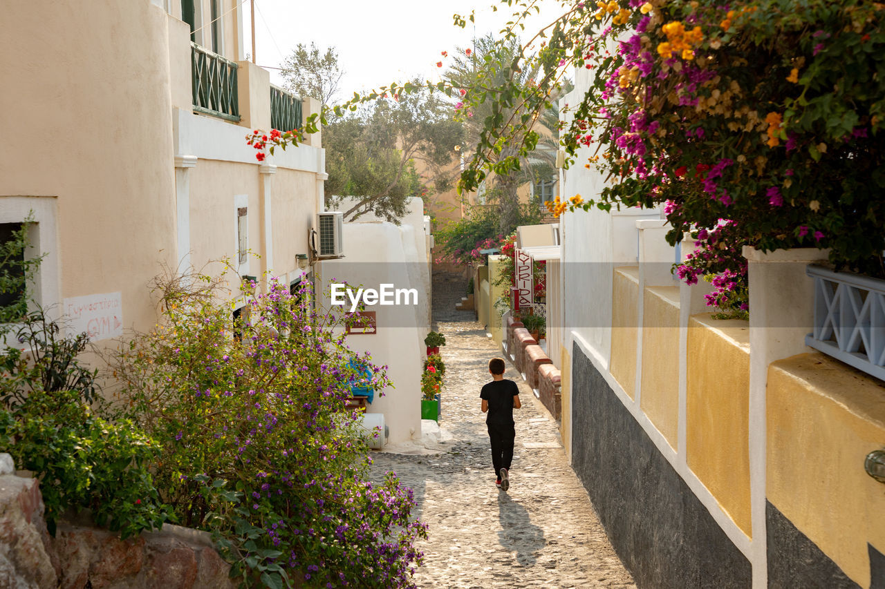 WOMAN WALKING BY FLOWERING PLANTS AGAINST BUILDING