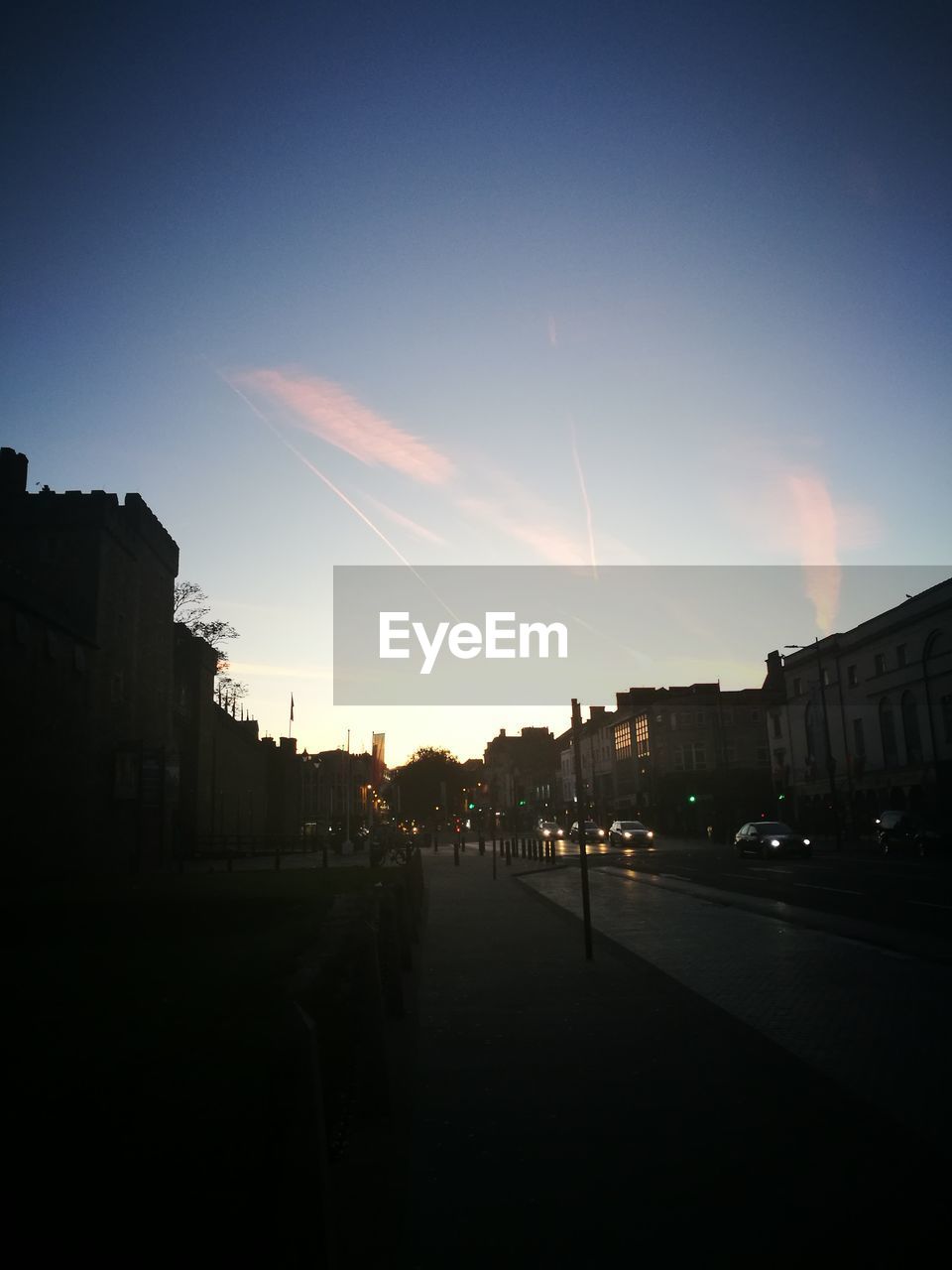 STREET AMIDST SILHOUETTE BUILDINGS AGAINST SKY DURING SUNSET