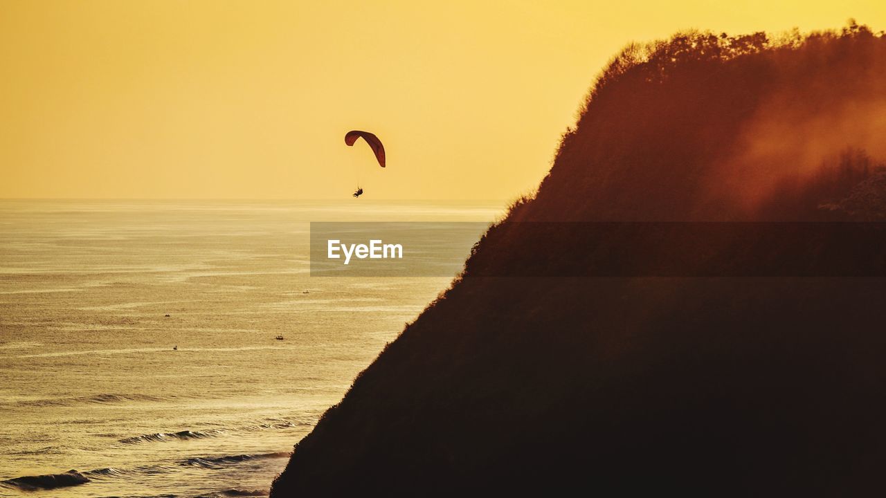 Scenic view of sea against sky with paragliding during sunset