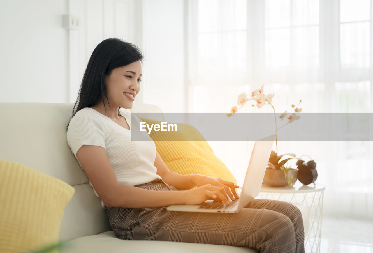 Young lady with modern laptop sitting on sofa at home