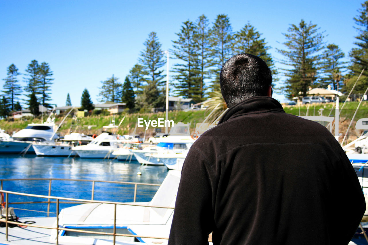 REAR VIEW OF MAN IN BOAT AGAINST TREES