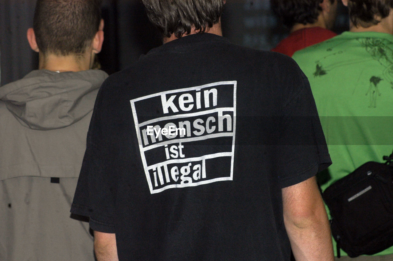 rear view, text, law, men, t-shirt, group of people, communication, sleeve, person, social issues, clothing, government, adult, police force