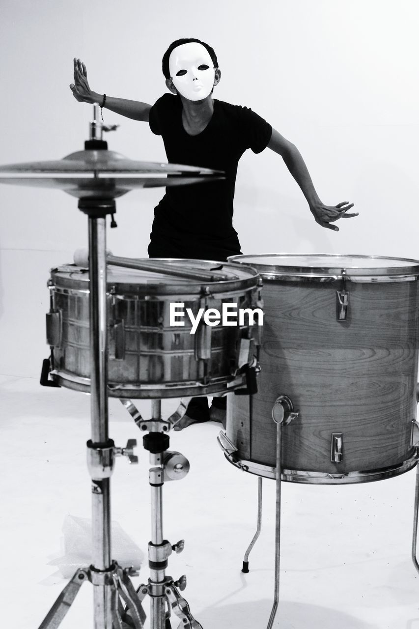 Man wearing mask standing by drum kit against white background