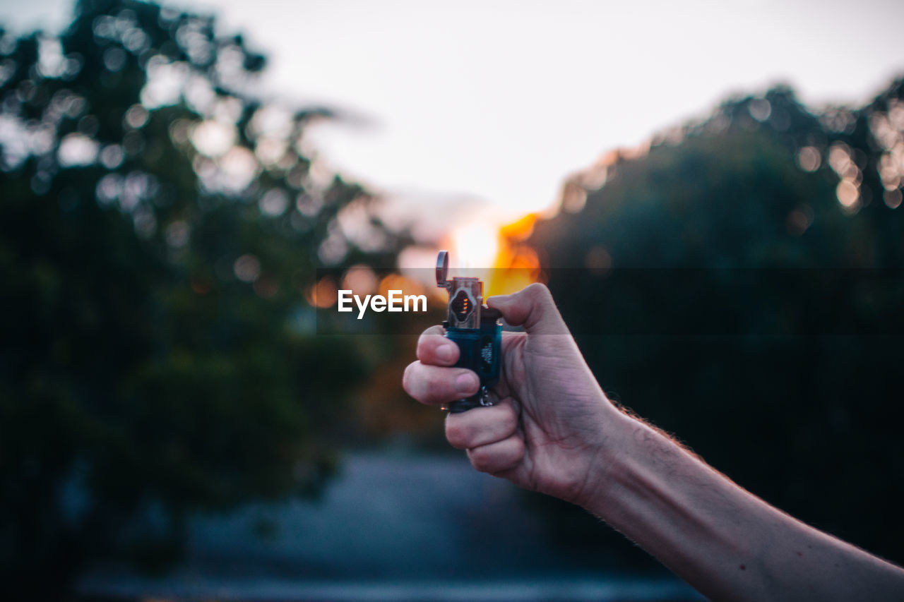 Close-up of hand holding illuminated light against sky during sunset