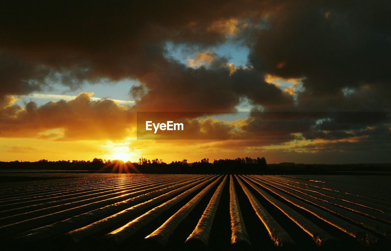 Farm against cloudy sky at sunset