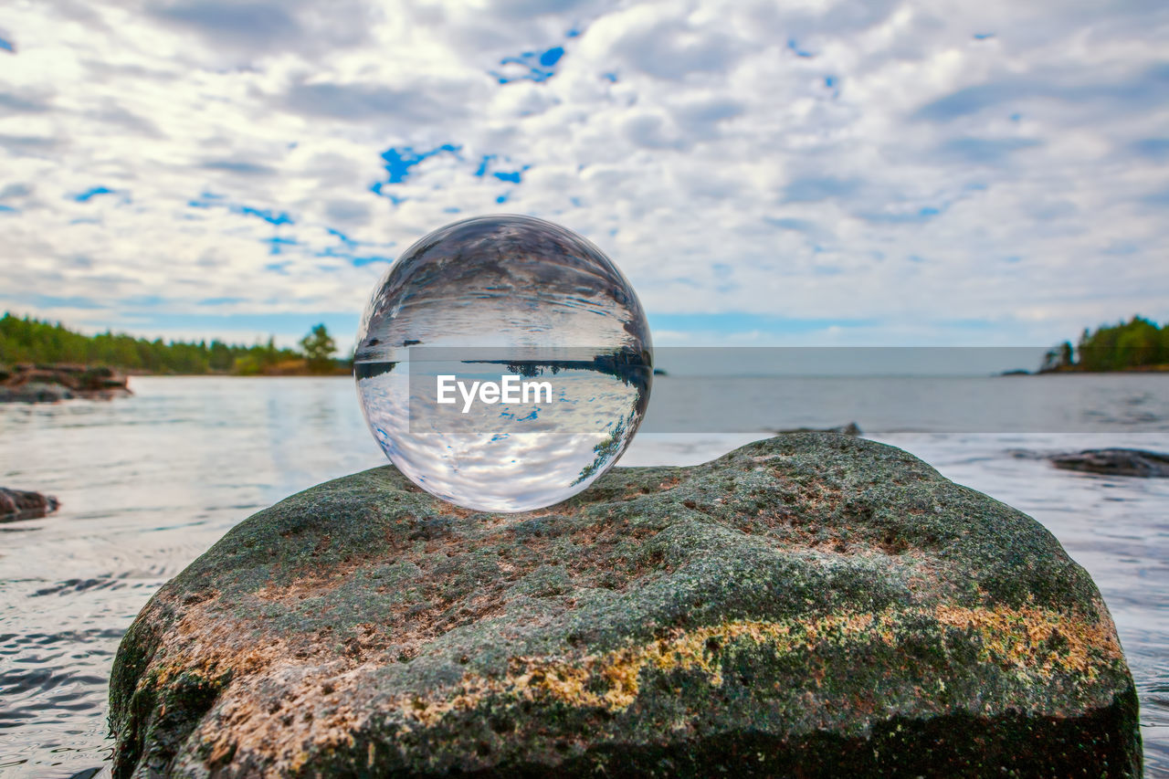 Close-up of crystal ball on rock by sea against sky